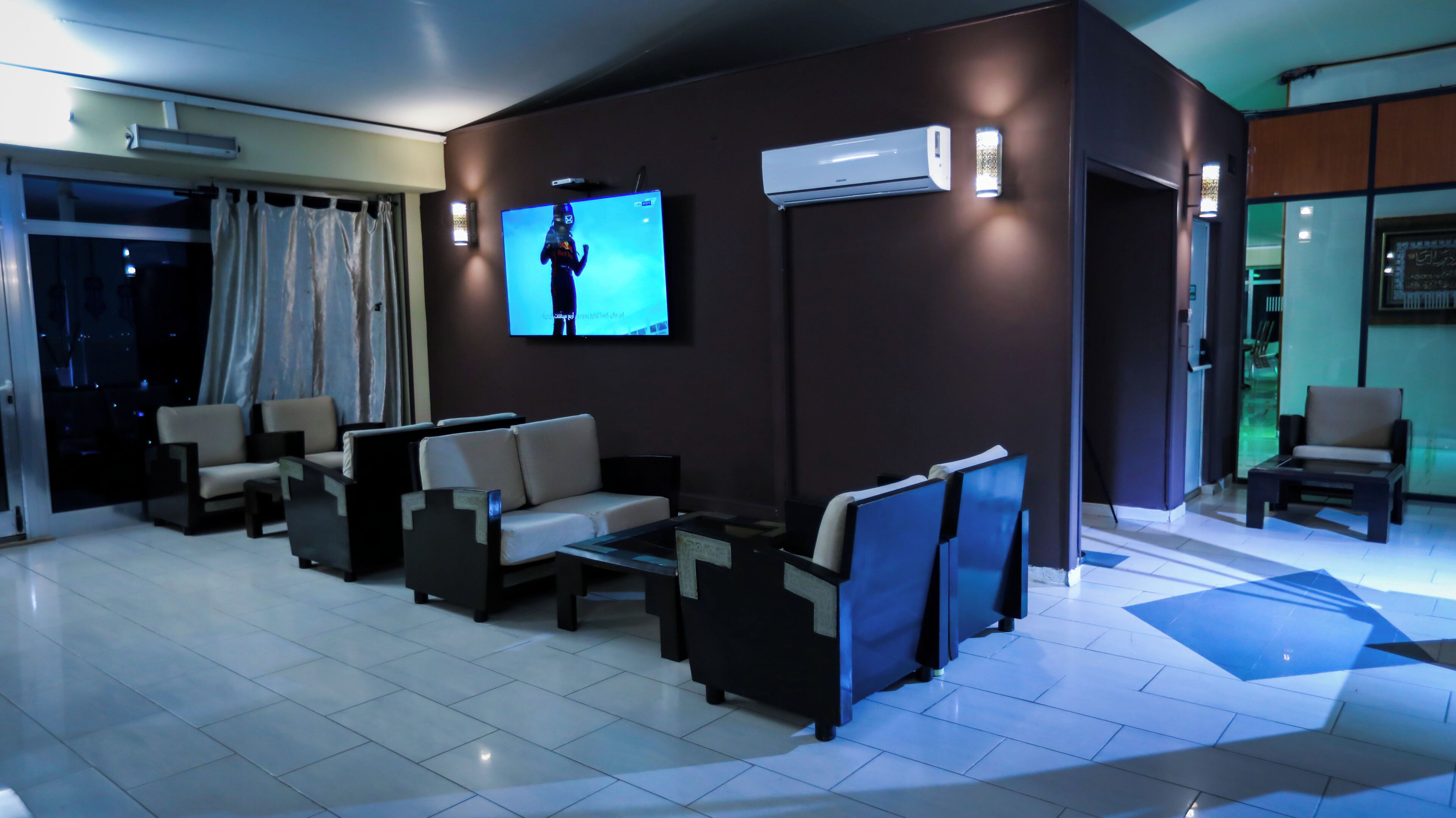 Eine Hotellobby mit Fernseher, Sitzgelegenheit, Klimaanlage und Blick durch eine Glastür.