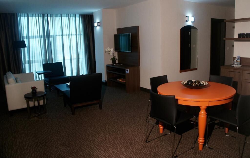 A hotel room with a living area, a dining table, a TV, a mirror, and a small side table.