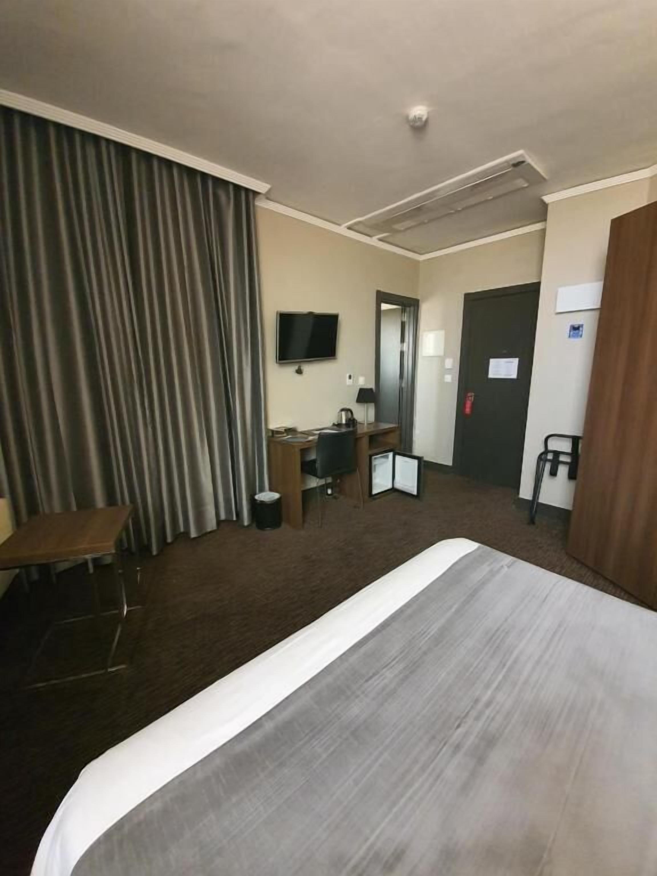 A hotel room with a large bed, a desk with a chair, a television, and a door.