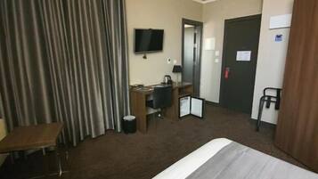 A hotel room with a large bed, a desk with a chair, a television, and a door.