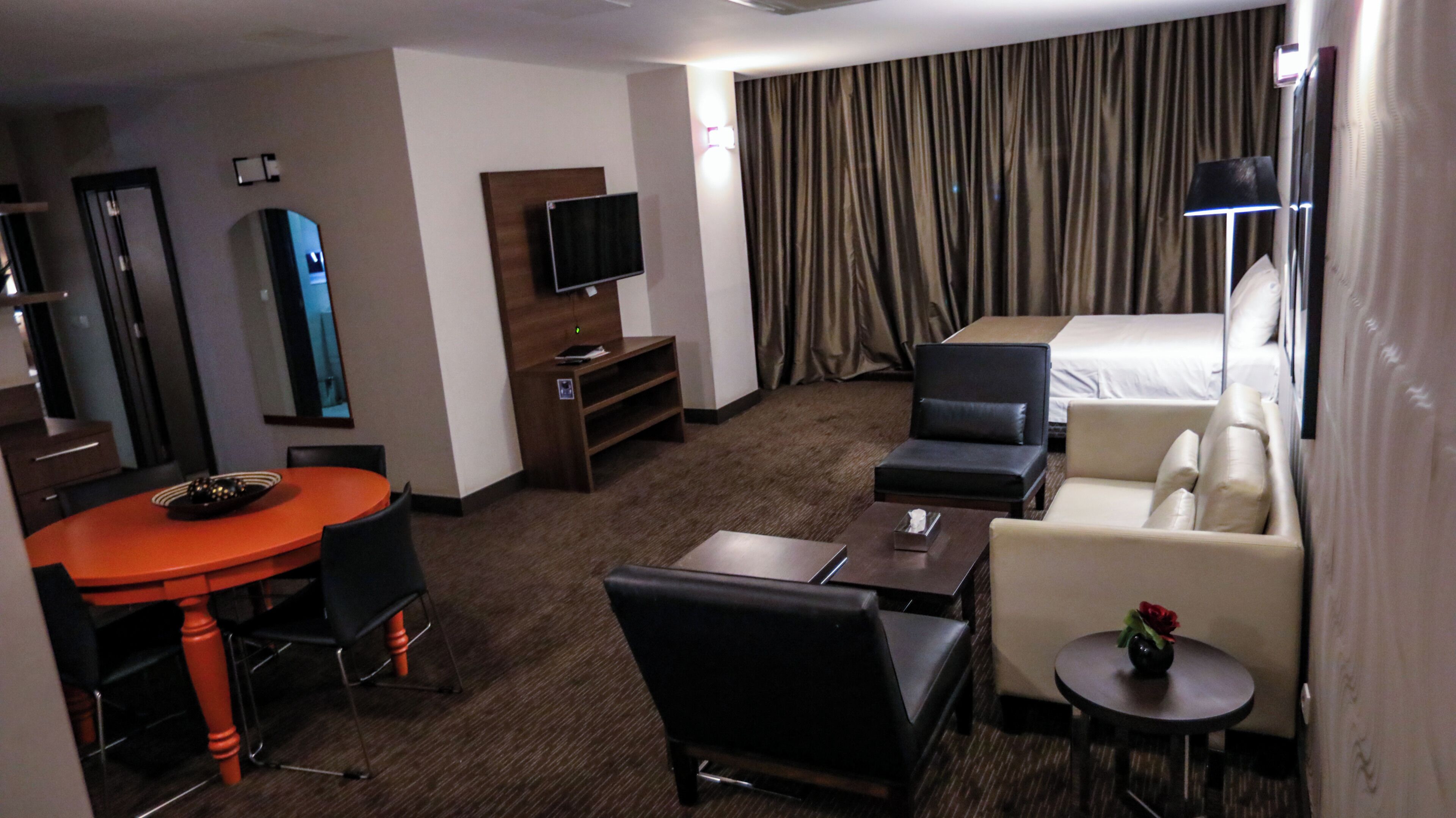 Una habitación de hotel con una mesa de comedor, dos sofás, un televisor y una cama.