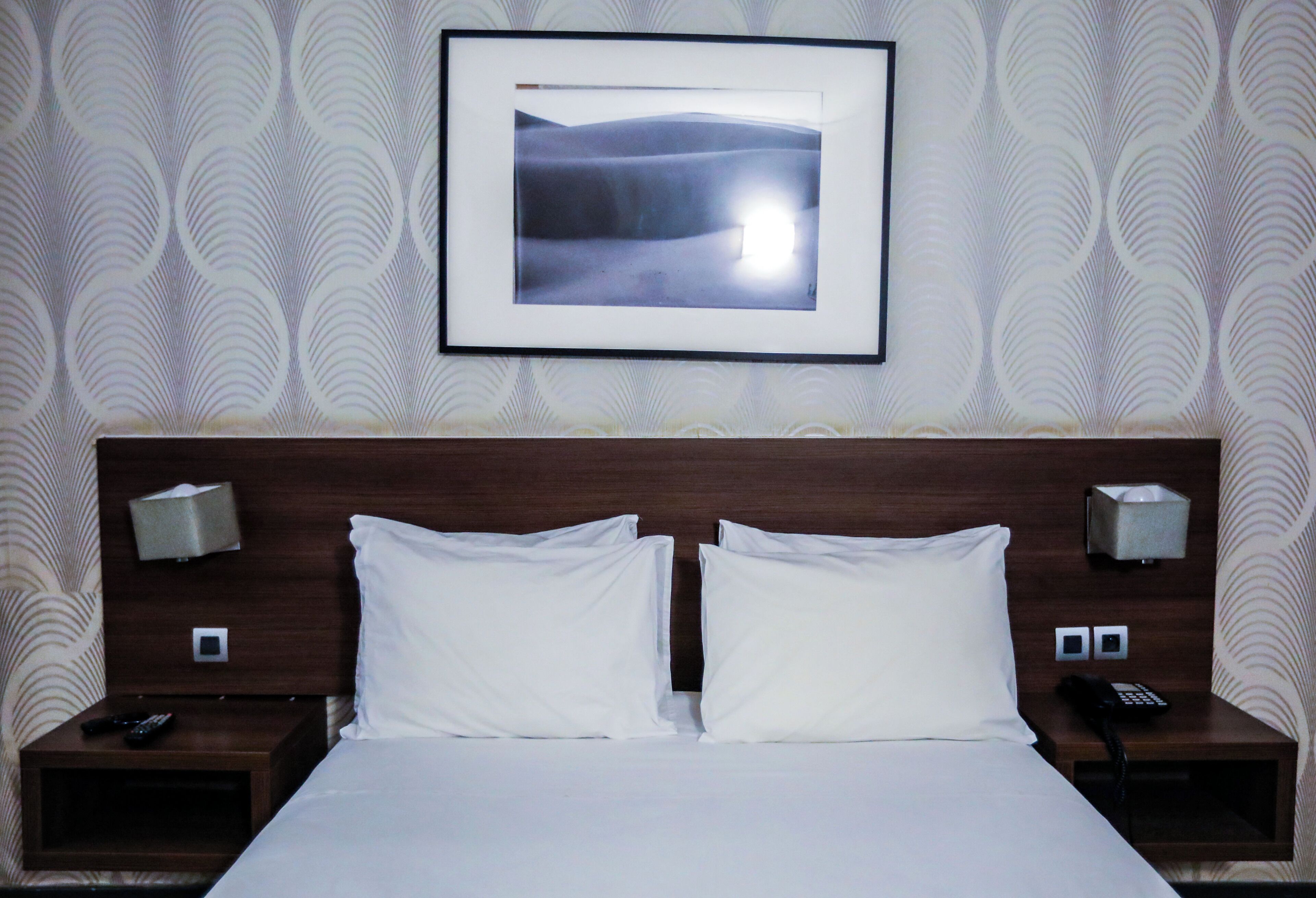 Camera d'albergo con un letto grande, due comodini, un quadro incorniciato appeso al muro e carta da parati decorata.
