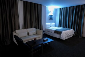 A hotel room with a bed, a sofa, a small table, and a bedside table.