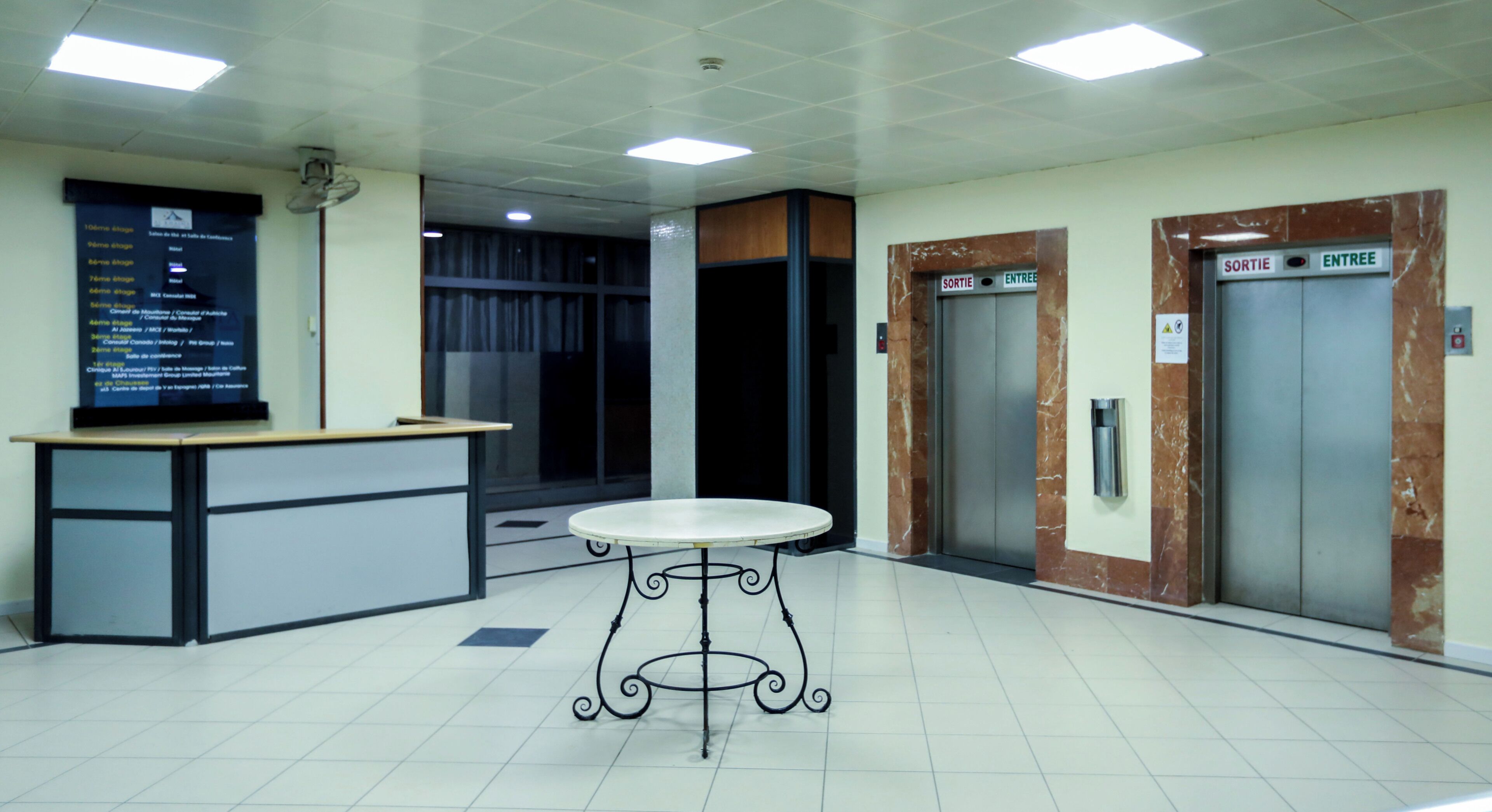 Un área de recepción con mostrador, una mesa y dos ascensores con indicaciones 'SORTIE' y 'ENTREE'.