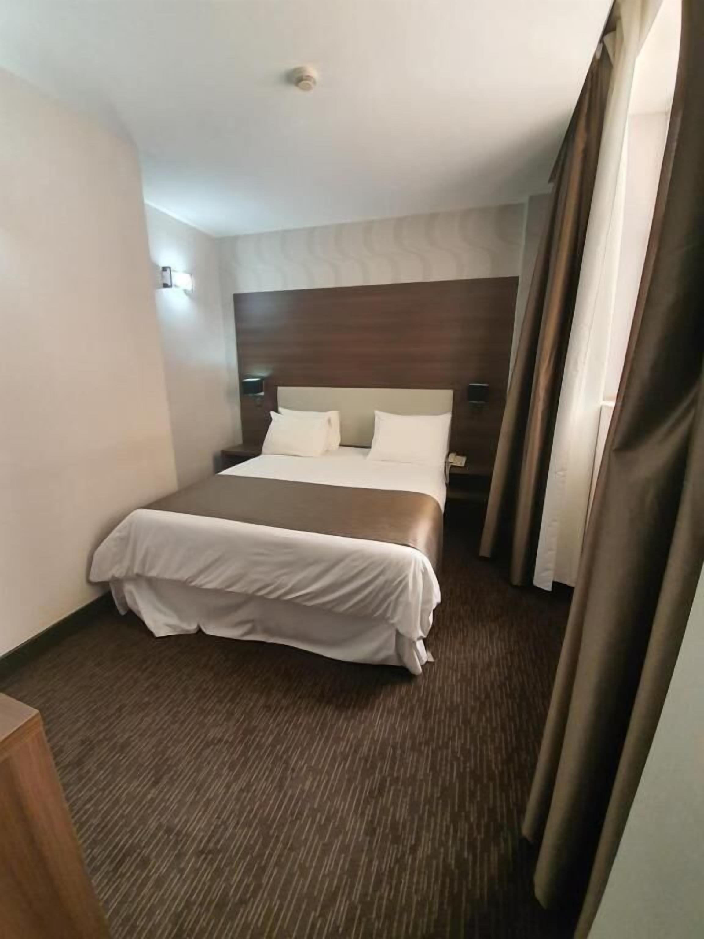 Habitación de hotel con una cama grande, un cabecero de madera, una mesita de noche y una cortina.