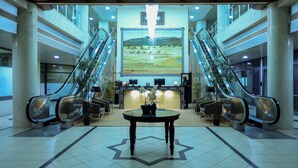 Un hall d’entrée doté de deux escaliers mécaniques, d’un comptoir de réception, d’une grande fresque murale et d’une table centrale dont le motif au sol est en forme d’étoile.