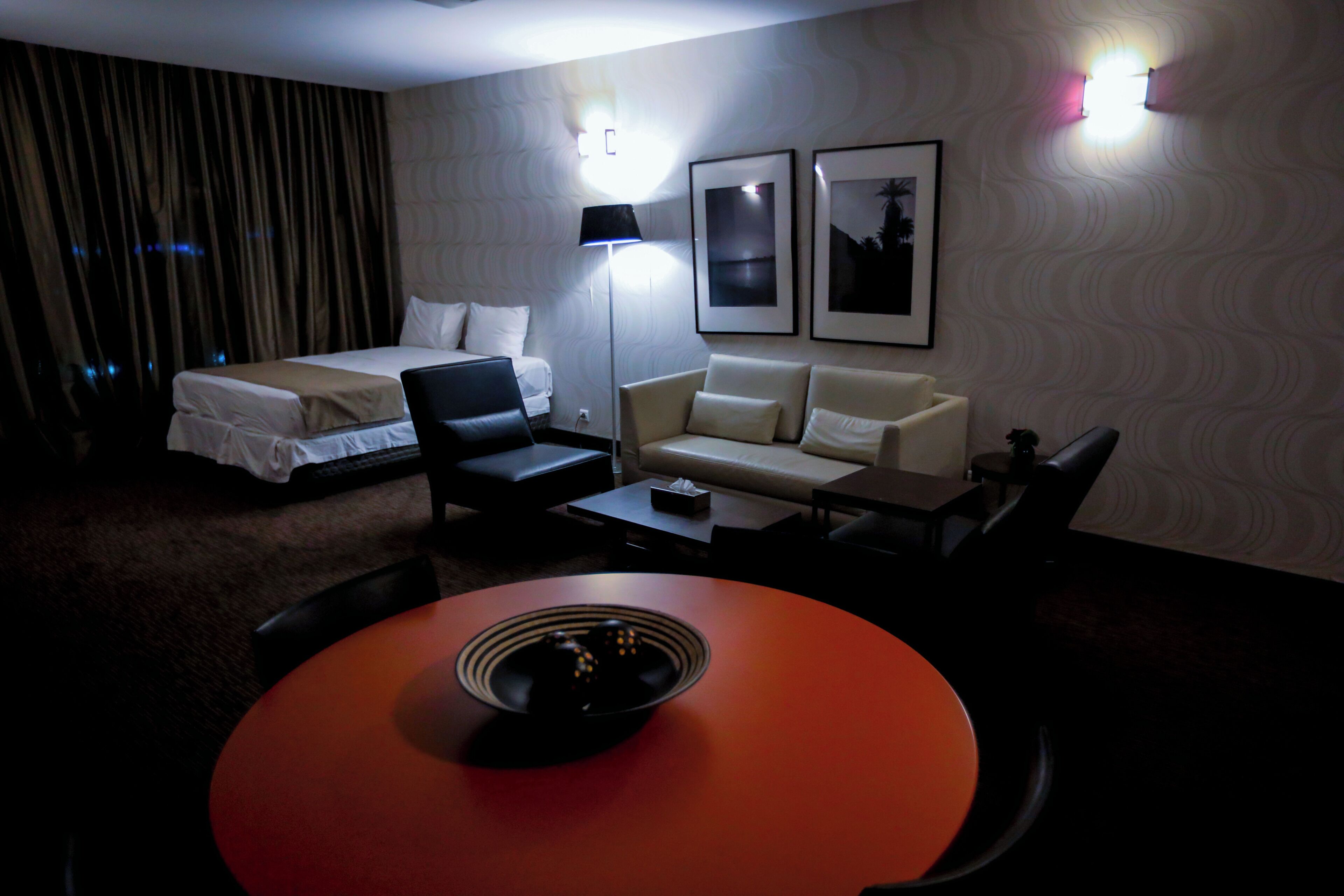 A hotel room with a bed, a sofa, a desk, a lamp, and two wall-mounted lights.