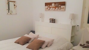 Ein ordentlich bezogenes Bett mit weißen und braunen Kissen, ein Nachttisch mit Lampe und ein kleiner Stuhl mit einem Teddybär.