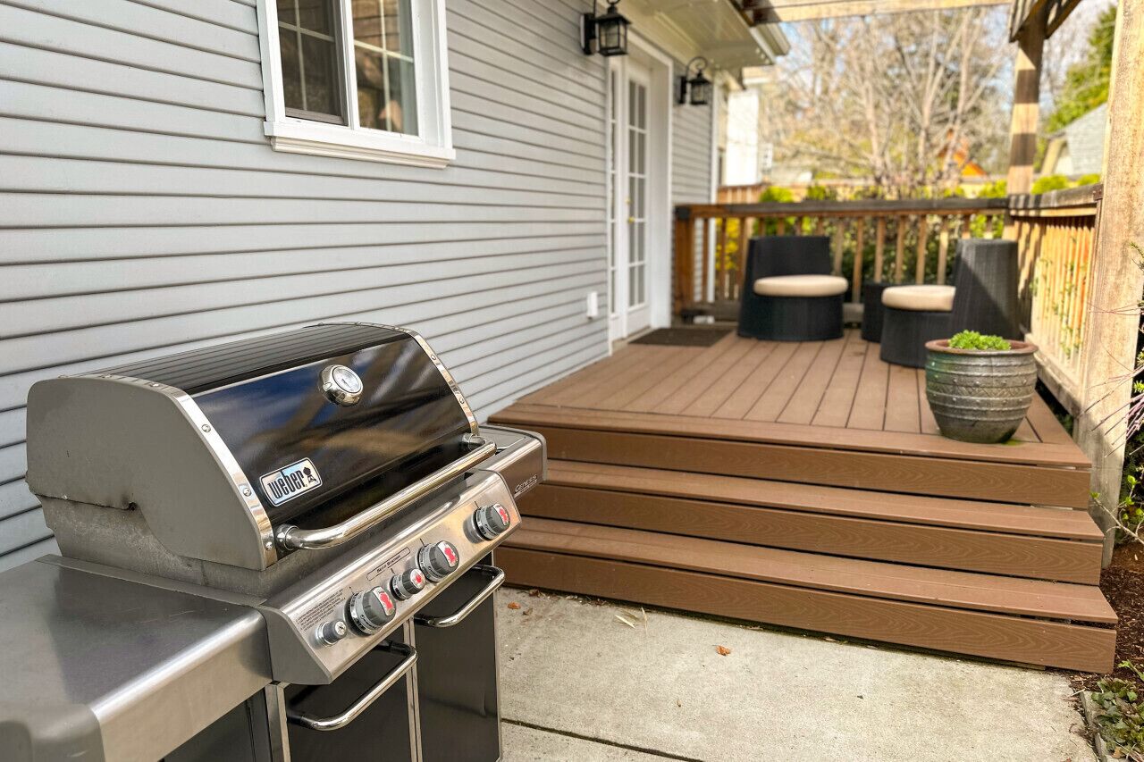 Una parrilla Weber sobre una terraza de madera con escalones que llevan a un porche.