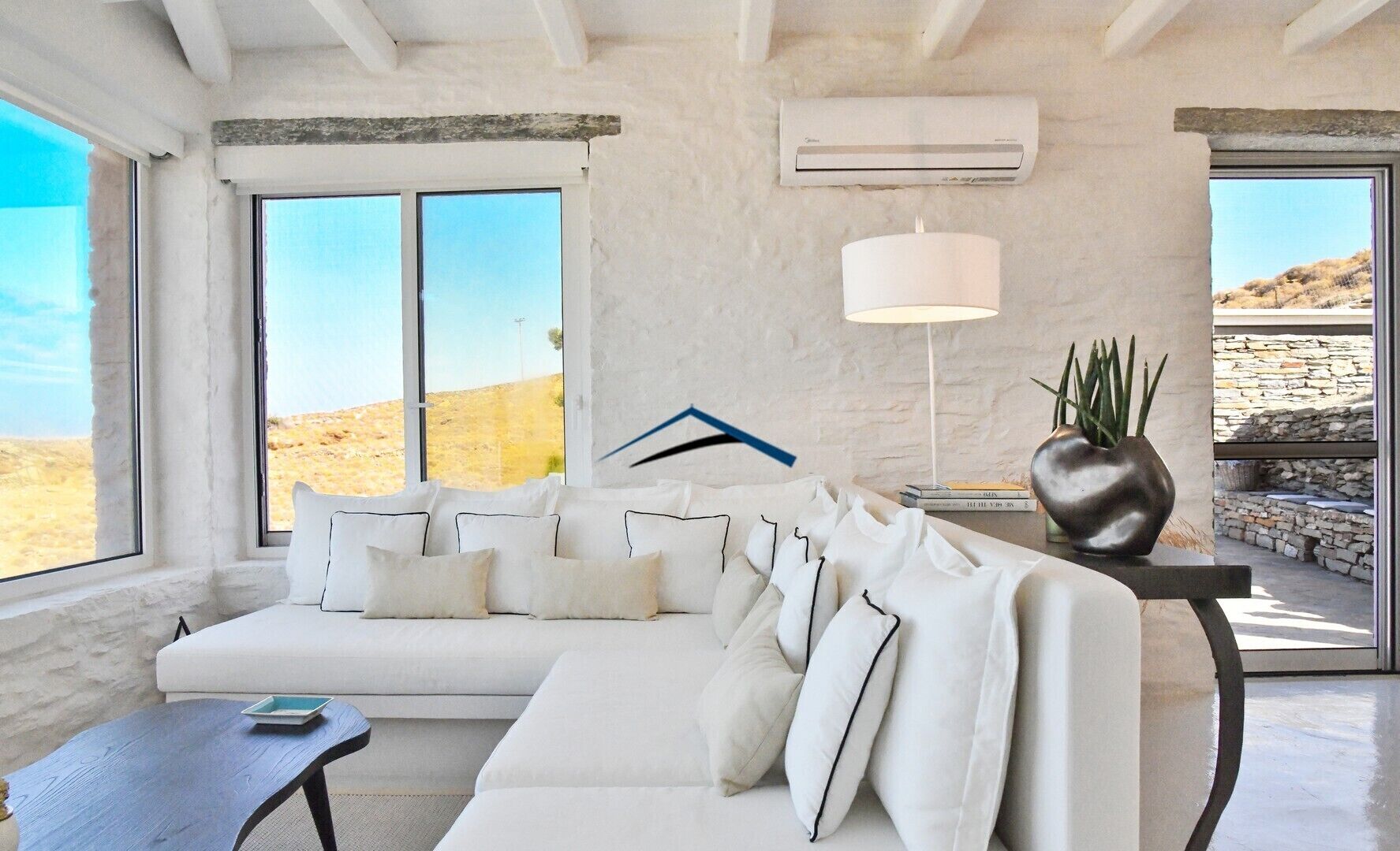 A modern living room with a white sofa, a table, and a lamp. There is a large window with a view of the desert.