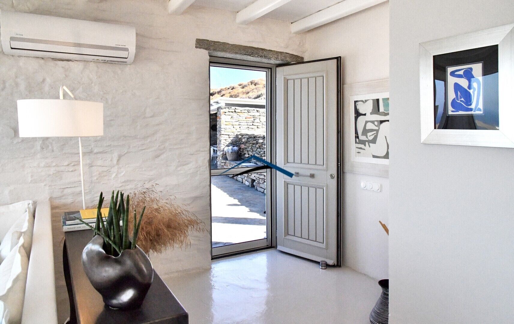A modern interior with a white wall, a door leading outside, and a vase with dried plants on a table.