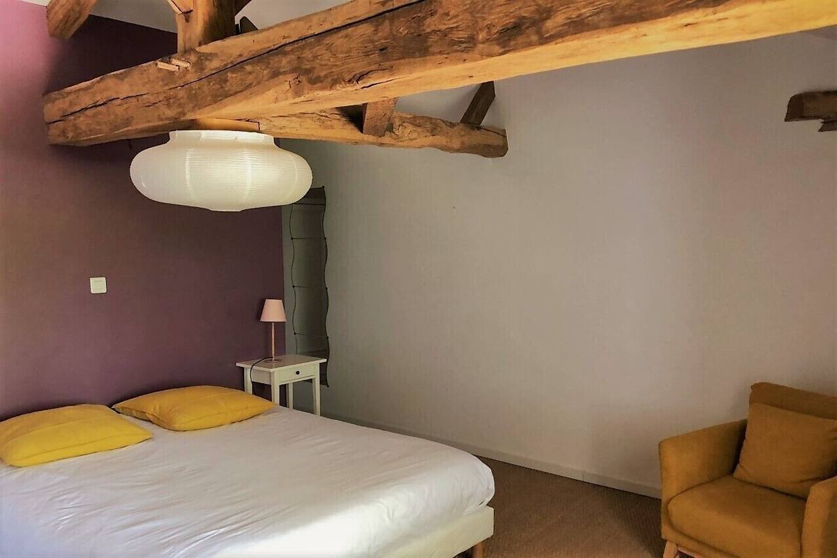 A bedroom with a bed, a chair, a small table, and a lamp.