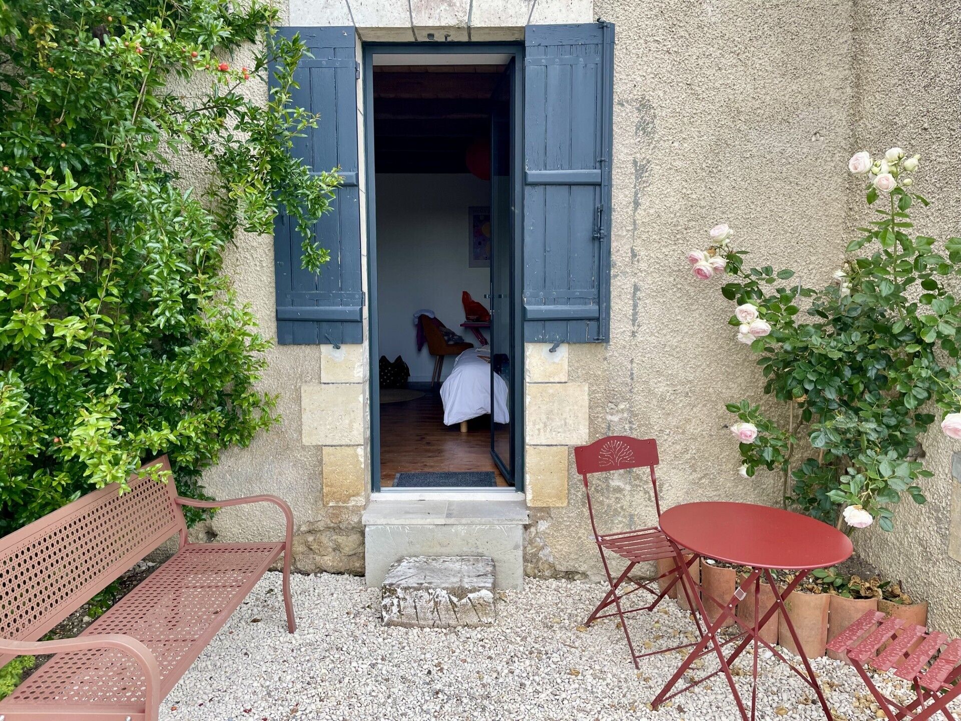 A rustic stone building with a wooden door, a bench, a folding table, and a chair outside.