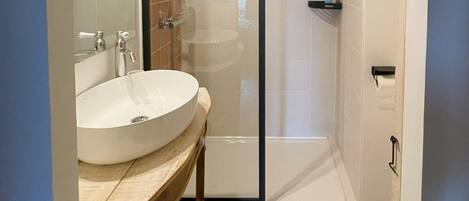A bathroom with a large white sink, a glass shower enclosure, and a tiled floor.