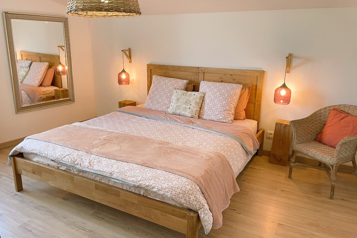A bedroom with a wooden bed, two nightstands, a wicker chair, and a mirror on the wall.