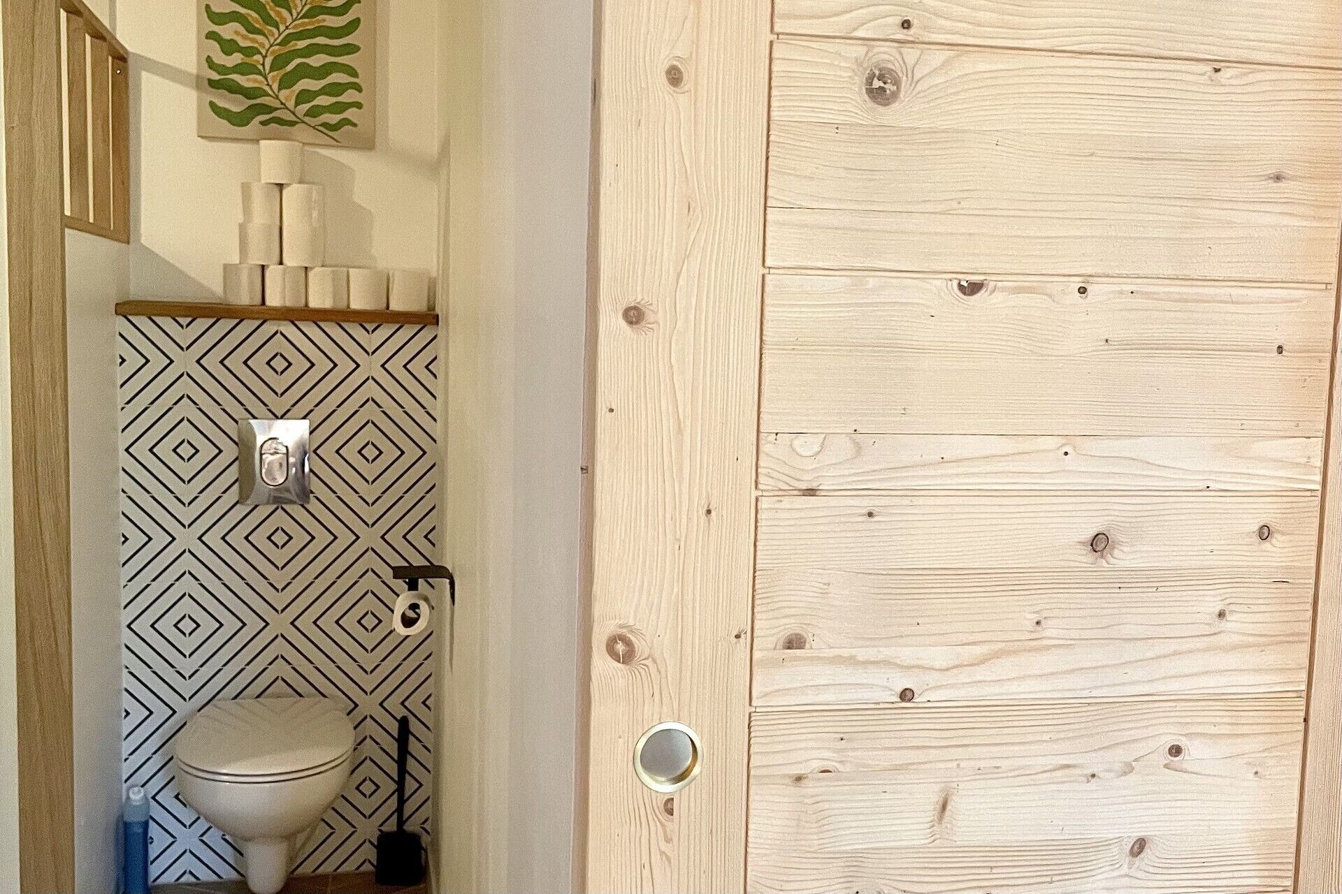 Ein Badezimmer mit Wandmuster, Toilette und Holztür.