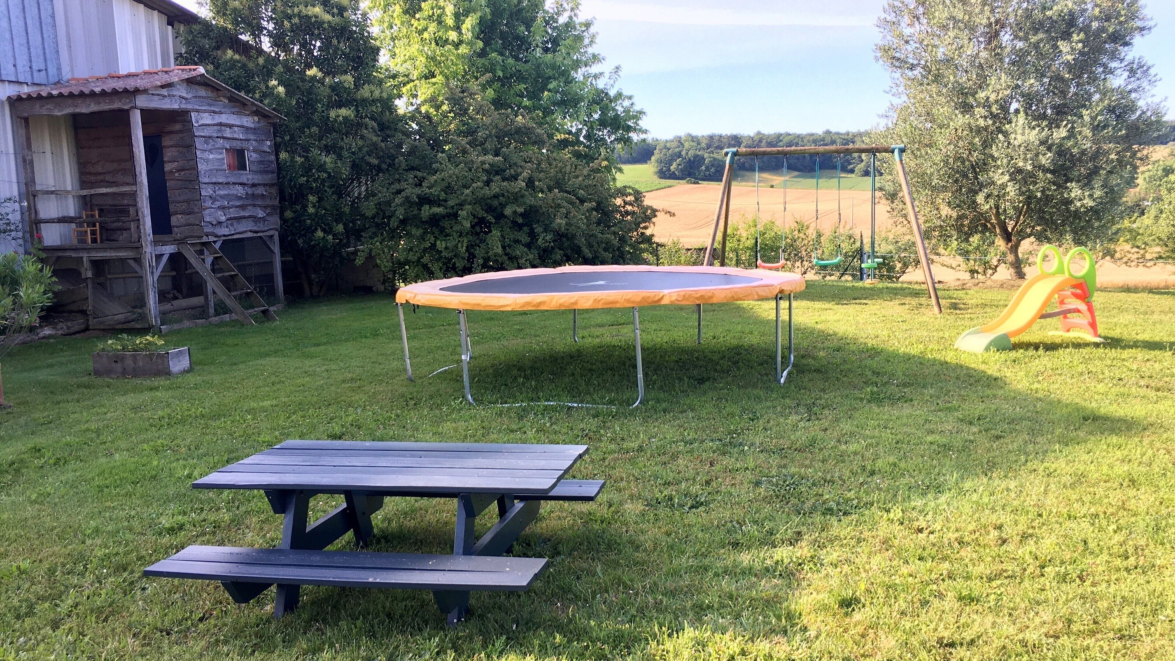 A grassy backyard with a trampoline, picnic table, and a swing set.