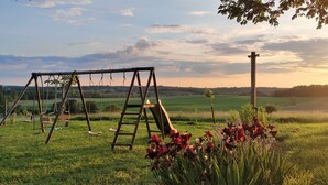 A swing set in a grassy field with a view of distant fields and a cloudy sky.
