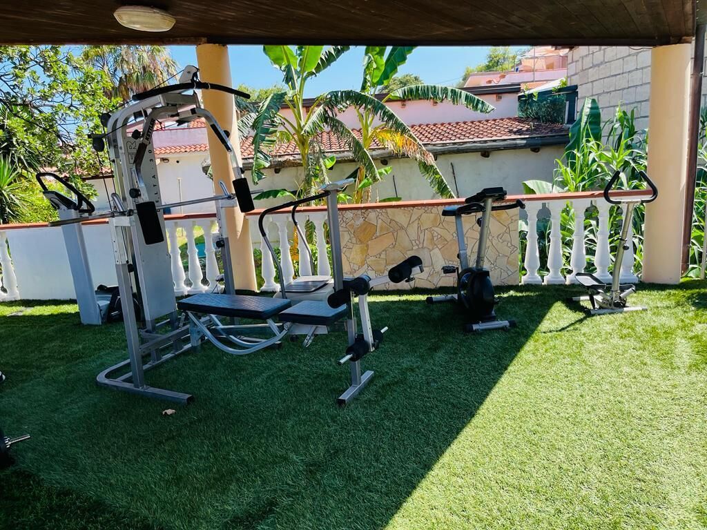 An outdoor gym with exercise equipment, a covered area, and a stone wall with plants.