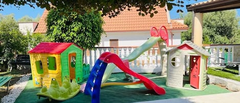 Un parque infantil con un tobogán, estructuras para escalar y una casita.