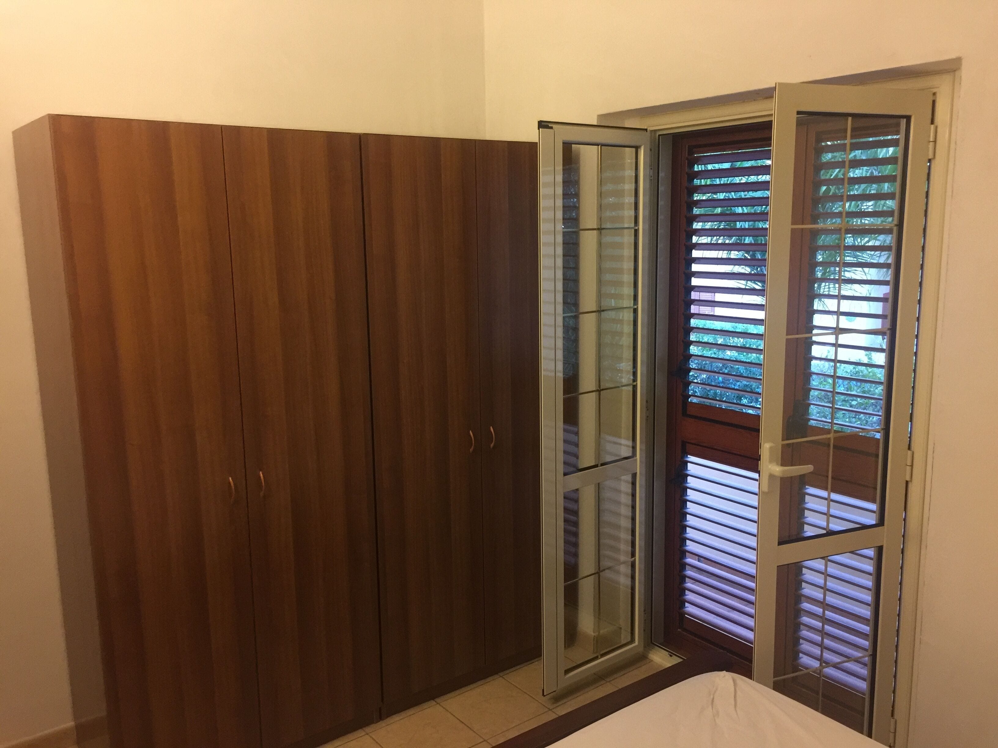 A room with a wooden wardrobe, a sliding glass door, and a bed.