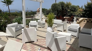 An outdoor patio area with white wicker furniture, a pergola structure, and a variety of plants. - Residence Villa Grazia  (Ricadi)