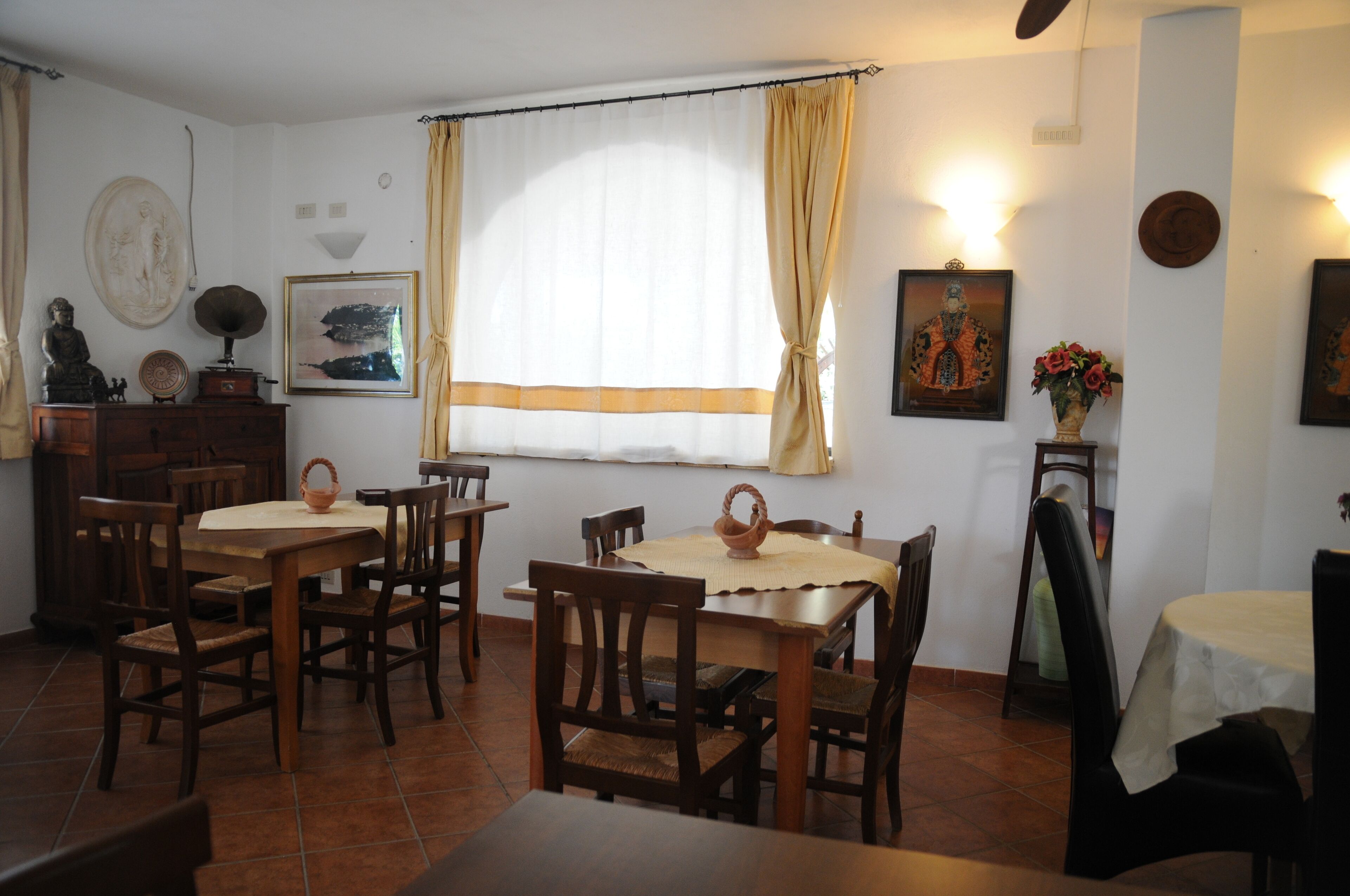 A dining area with wooden tables and chairs, a large window with curtains, and wall-mounted artwork.