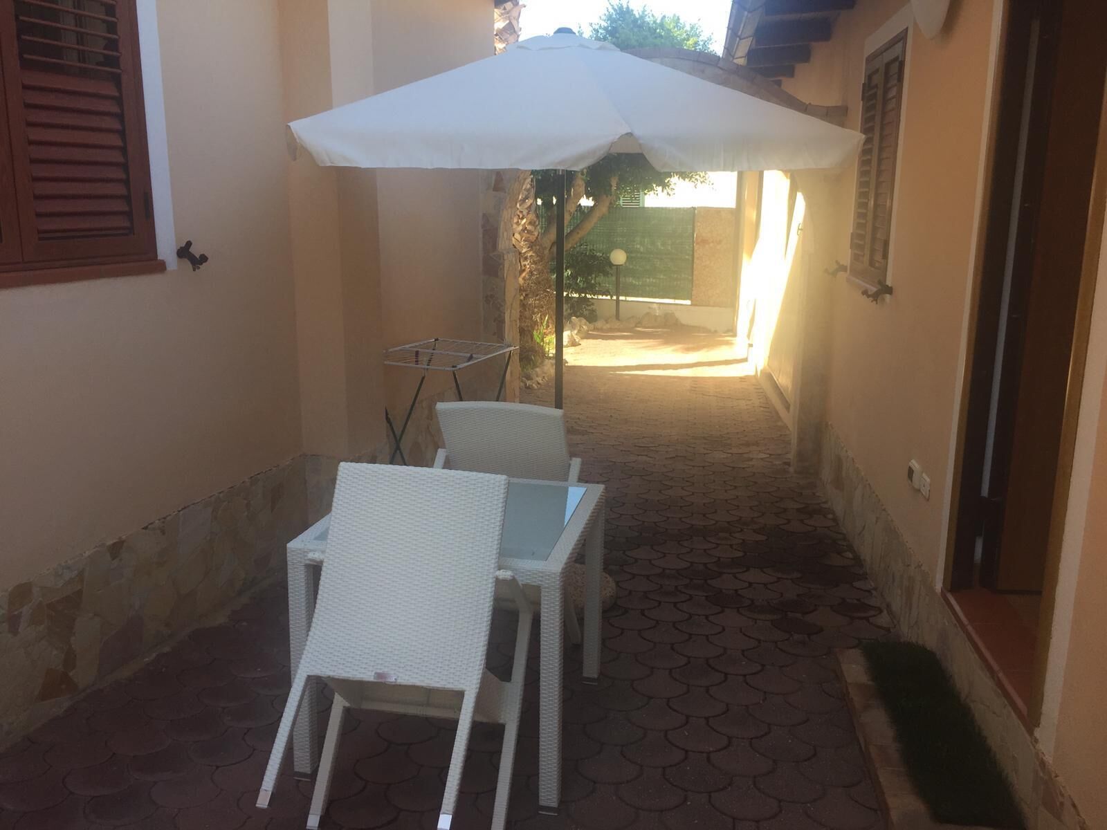 Eine schmale Terrasse im Freien mit einem weißen Sonnenschirm, zwei weißen Korbstühlen und einem kleinen Tisch.