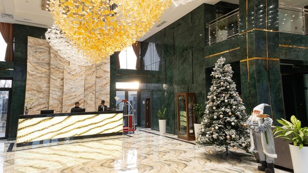 A lobby with a marble reception desk, a large decorative chandelier, a Christmas tree, and a gnome figure.