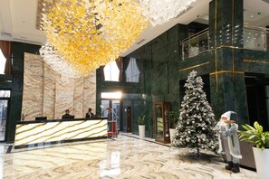Un hall d’entrée avec un comptoir de réception en marbre, un grand lustre décoratif, un sapin de Noël et une figurine de gnome.