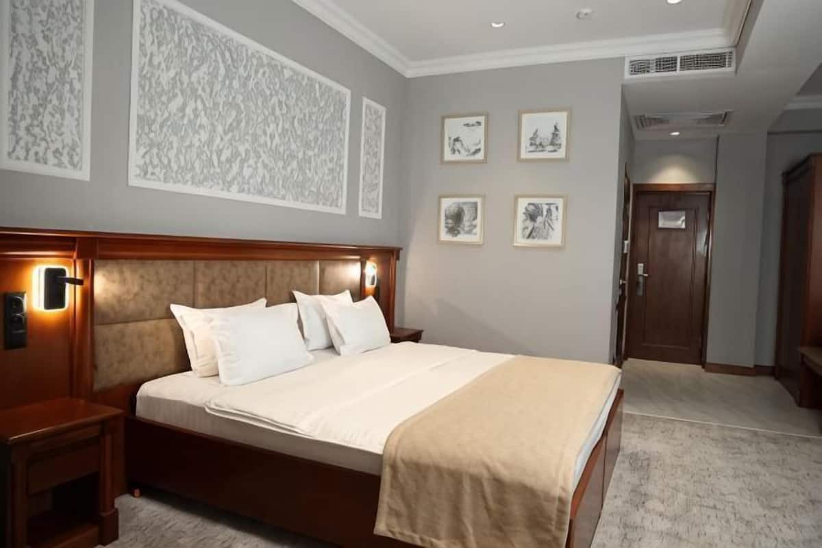 Ein Hotelzimmer mit einem großen Bett, einem Nachttisch, einem Holz-Kopfteil und gerahmten Kunstwerken an den Wänden.