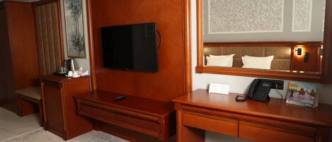 A hotel room with a wooden desk, a flat-screen TV, a telephone, and a mirror.