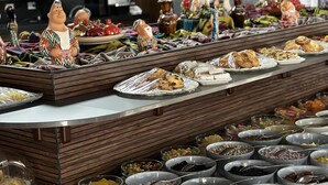 A buffet with various food items, including pastries, fruits, and nuts, arranged on a counter with decorative figurines.