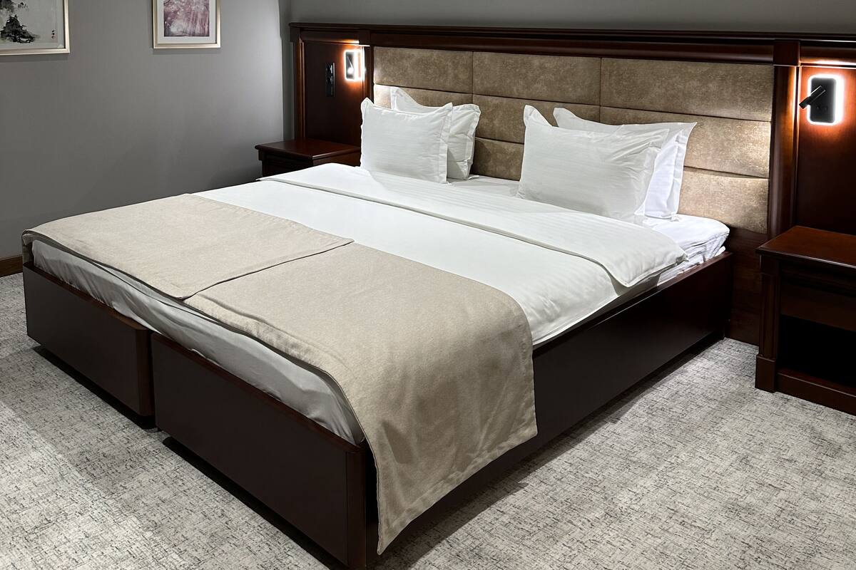 Ein ordentlich eingerichtetes Schlafzimmer mit einem großen Bett, gerahmten Kunstwerken an den Wänden und einem Kopfteil mit integrierter Beleuchtung.