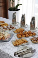 Una mesa de buffet con diversos pasteles y sándwiches, dispensadores de condimentos de plata y una planta en maceta al fondo.