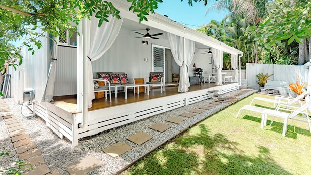 A covered outdoor seating area with a ceiling fan, white curtains, and a patio with a fire extinguisher. - Spa,Fire Pit,Cinema - The Cottage Coolum Beach (Coolum Beach)