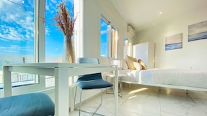 A modern hotel room with a large bed, a desk with a chair, and a view of the sky through large windows. - Phaedrus Living Luxury Flat Lighthouse75 (Paphos)