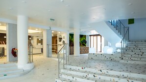 A modern hotel lobby with a central staircase, a reception desk, and a decorative wall.