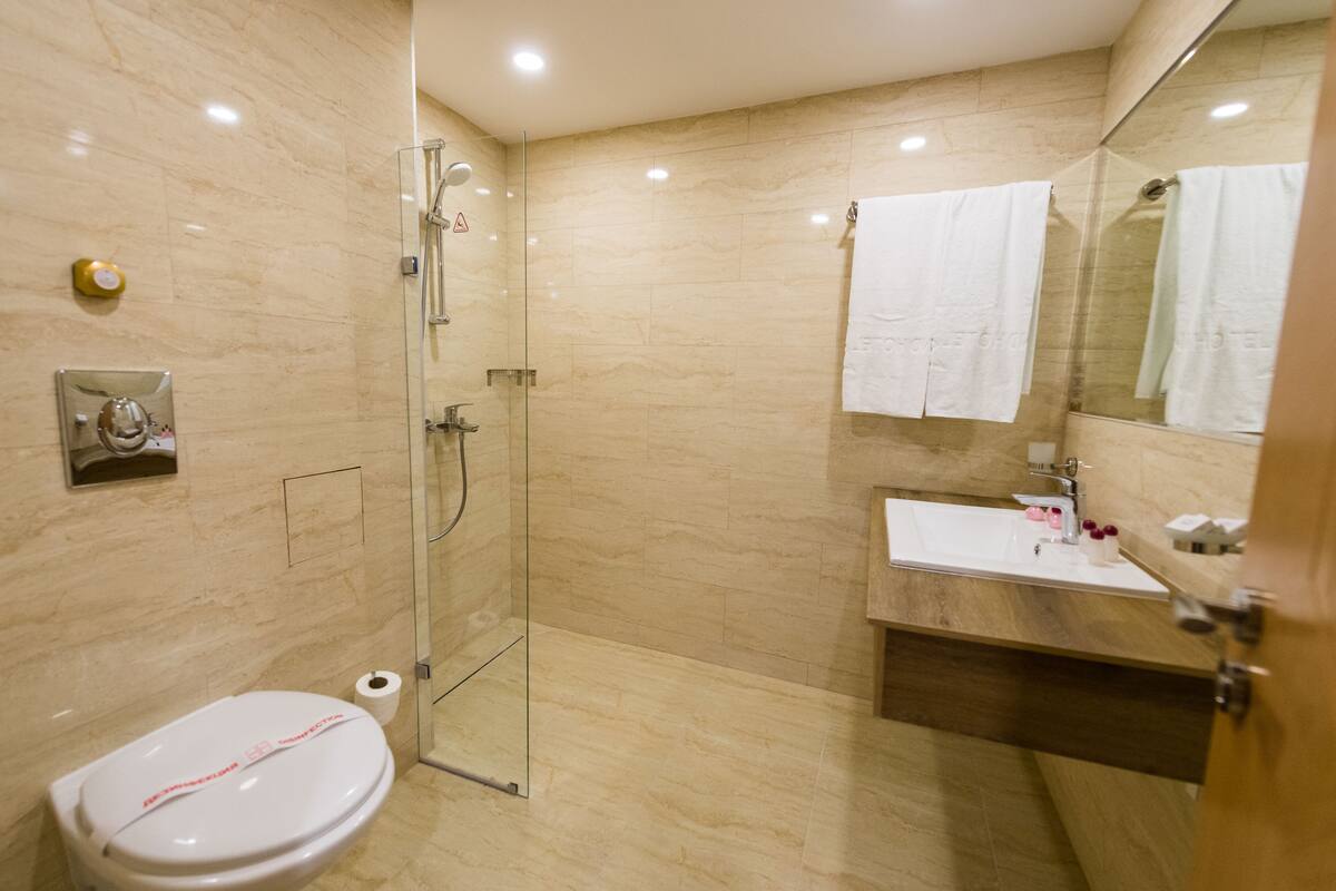 Un baño moderno con ducha acristalada, inodoro blanco, lavamanos con tocador de madera y espejo con una toalla colgando.
