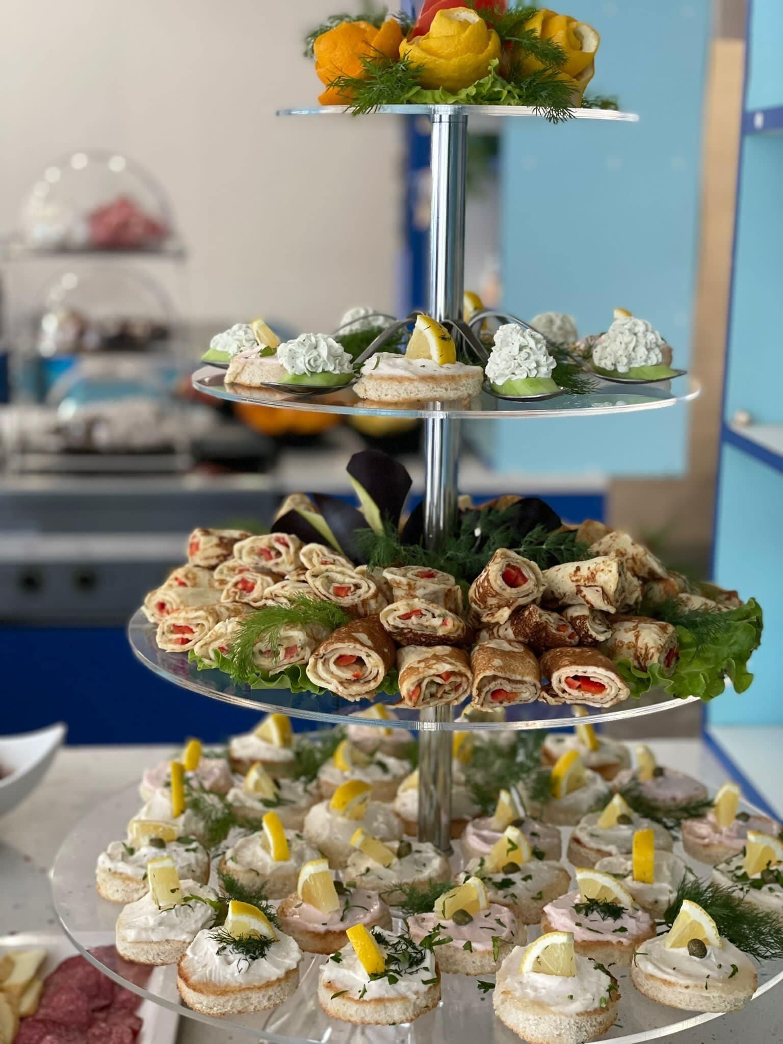 Un elegante platón escalonado con diversos aperitivos, como sándwiches, canapés y preparaciones decoradas, presentado en estilo bufé.