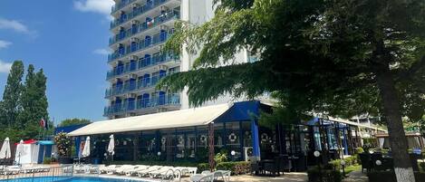 Un hotel con piscina, mobiliario exterior y un edificio grande con balcones.
