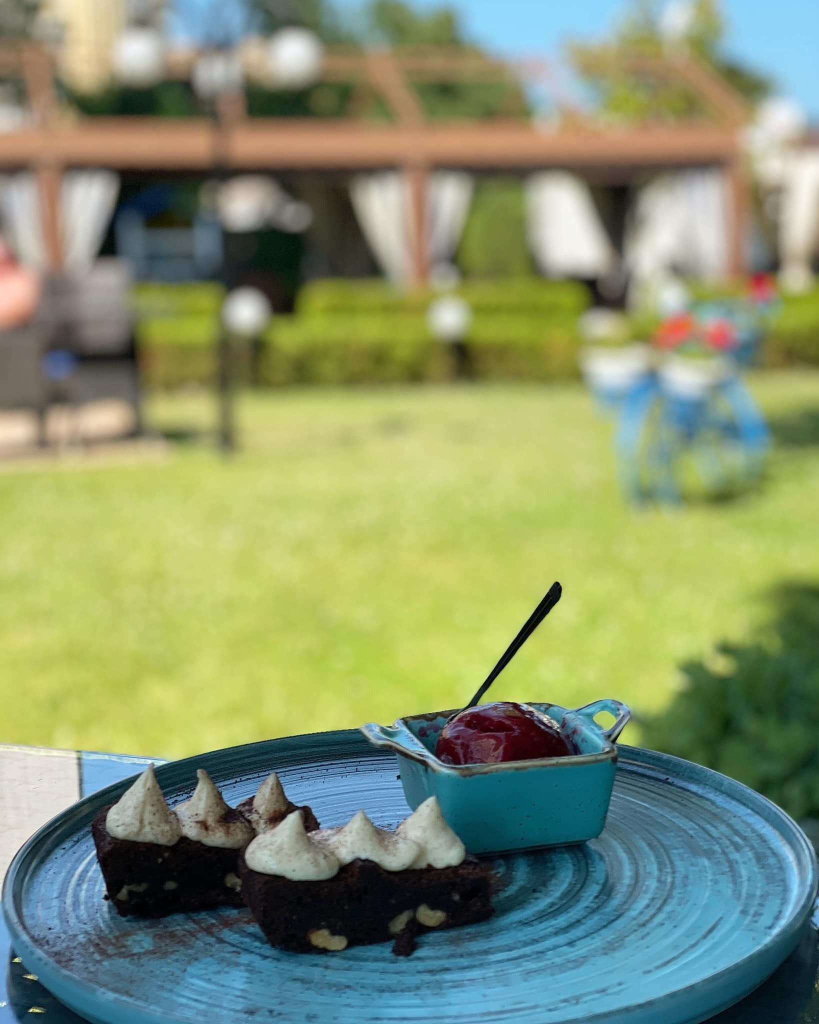 A dessert plate with a blue ceramic bowl containing a red sauce and a spoon, placed on a blue ceramic plate.