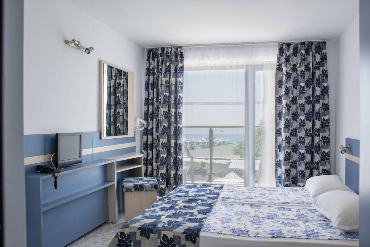 Habitación de hotel con cama, escritorio con computadora, una silla y balcón con vista al mar.