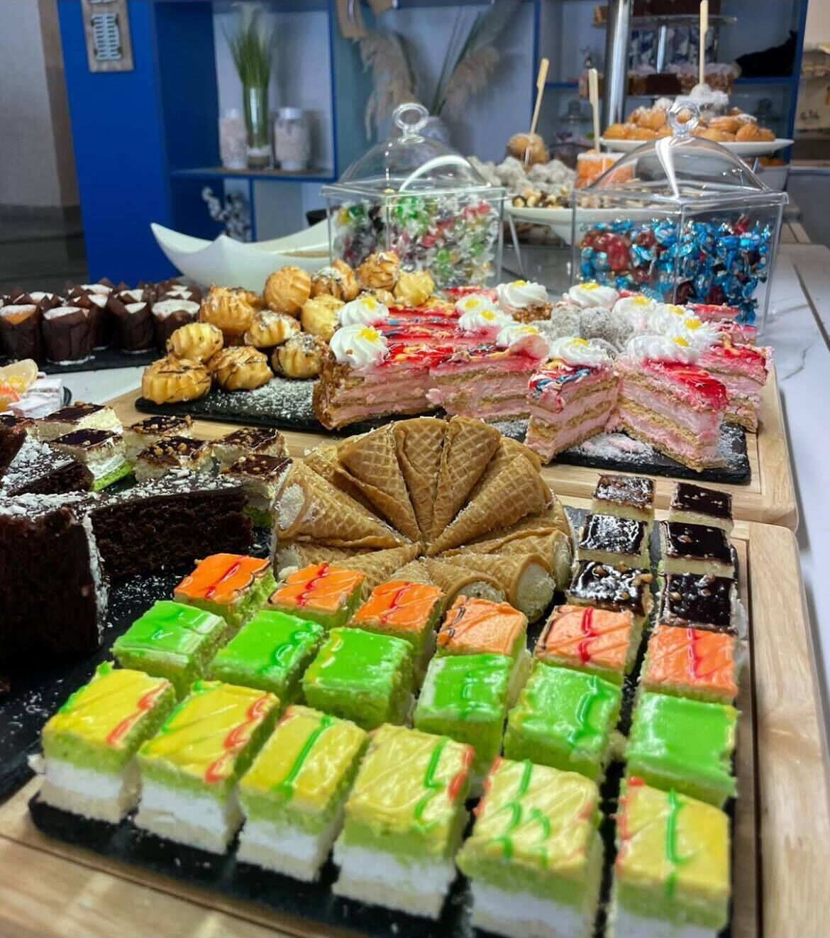 Una variedad de postres en una mesa buffet, incluyendo pasteles, productos de repostería y cuadrados de gelatina de colores.