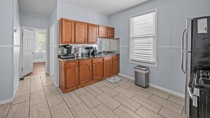 A modern kitchen with wooden cabinets, a stainless steel refrigerator, and a window with blinds. - Dog-Friendly | Yard & Office (St. Louis)