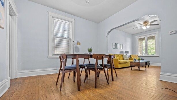 A spacious living room with hardwood flooring, a dining area with wooden chairs, a yellow sofa, and a ceiling fan. - Dog-Friendly | Yard & Office (St. Louis)