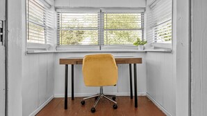 A room with a wooden desk, a yellow chair, and two windows with blinds. - Dog-Friendly | Yard & Office (St. Louis)