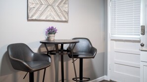 Une pièce avec une porte blanche, une table ronde avec deux chaises, et un élément décoratif mural au-dessus de la table.