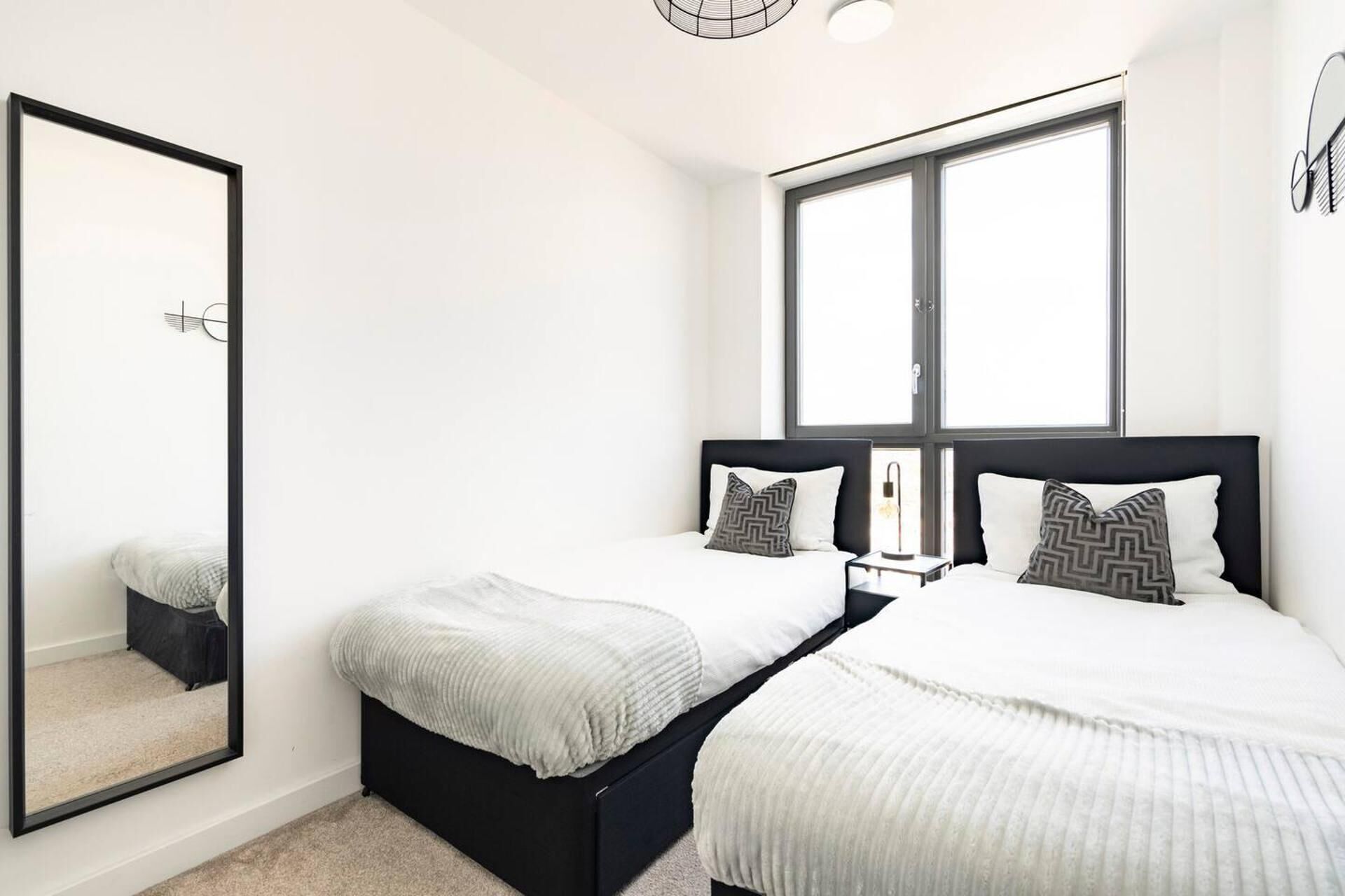 A modern bedroom with two beds, a large mirror, and a window.