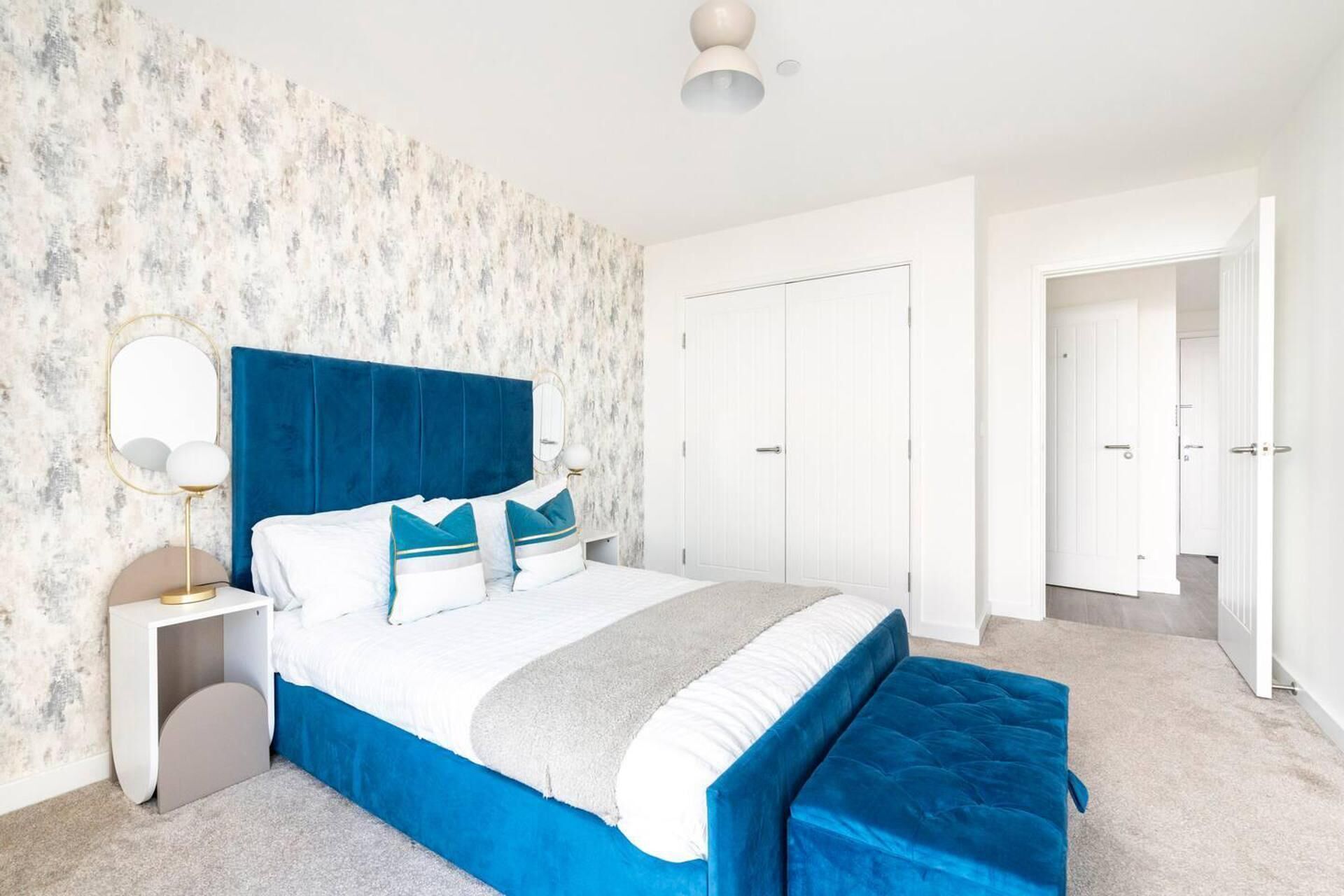 A bedroom with a large bed, a nightstand, a mirror, and a wardrobe.